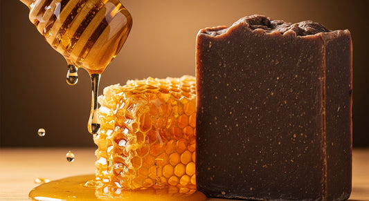 A close-up of a honey dipper dripping honey onto a honeycomb, next to a bar of dark brown African black soap, highlighting natural skincare ingredients.